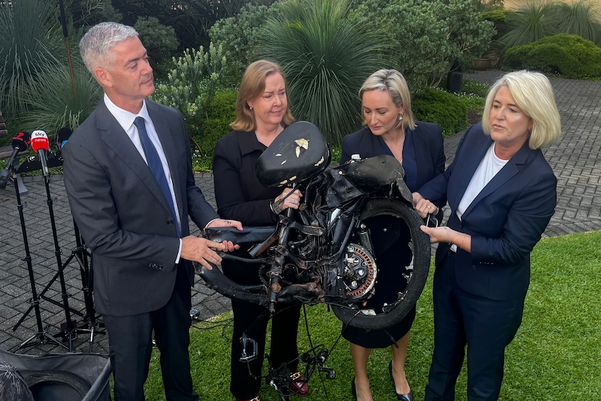 Ministers hold crushed e-bike on grass