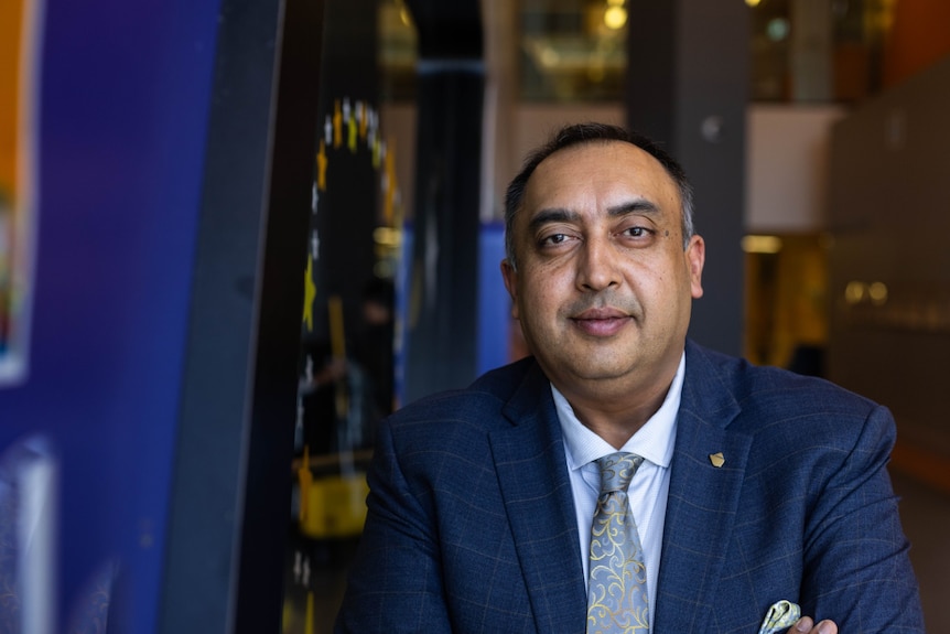 A man in a suit poses for a photo with a serious expression on his face.