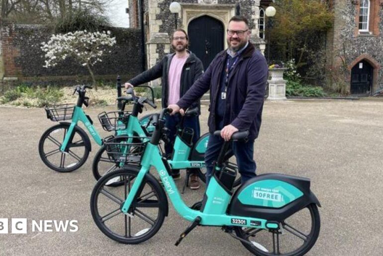 Two men stood next to three turquoise e-bikes.