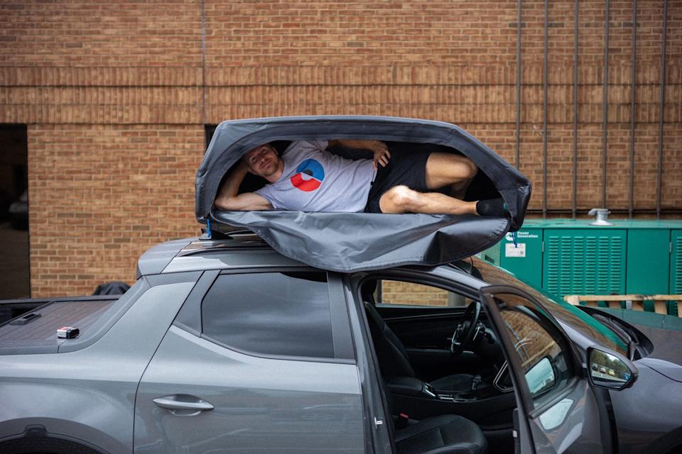 person inside a rooftop cargo carrier mounted atop a grey vehicle