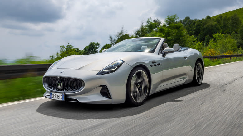 A silver Maserati Gran Turismo Folgore convertible being driven on a mountain road with greenery in the background.
