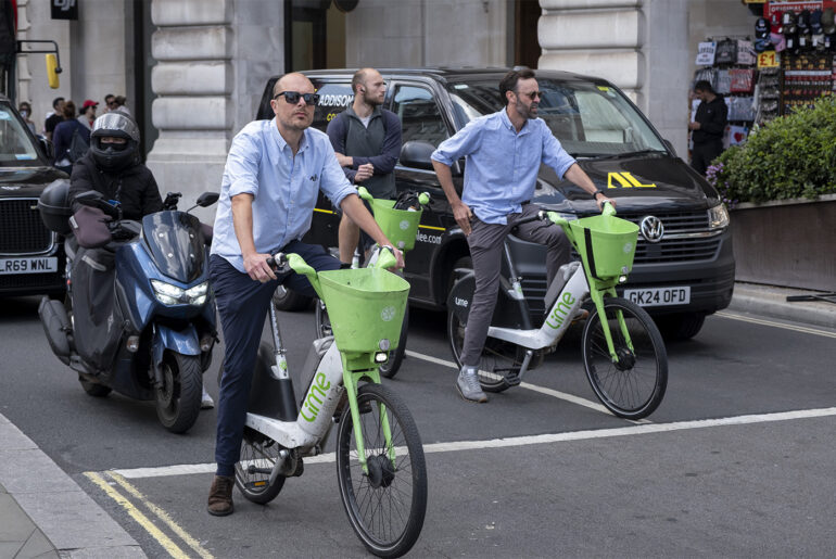 Men on Lime electric bicycles shown waiting at a traffic light.