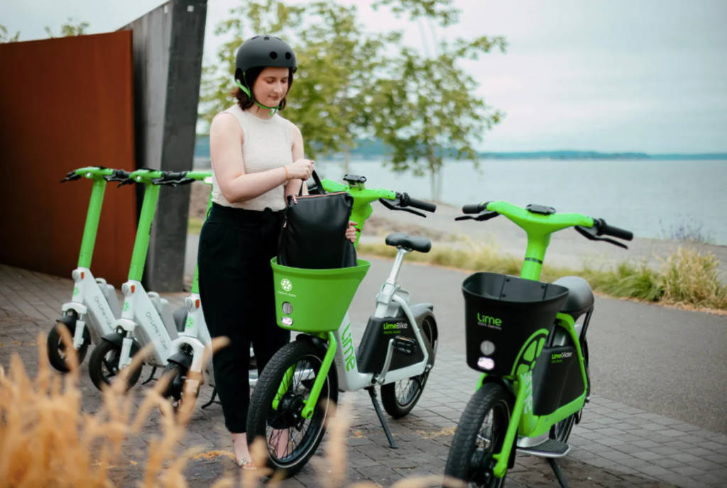 Image shows a woman unlocking a Lime LimeGlider scooter vehicle. 