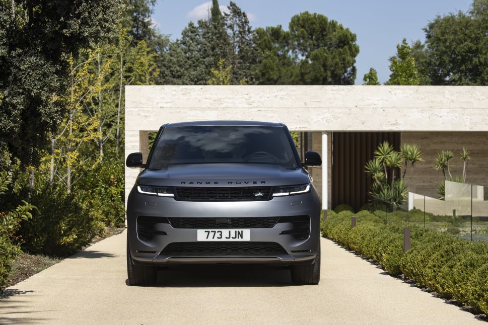 An exterior view of a silver Range Rover parked in front of a modern, minimalist building with a landscaped driveway.