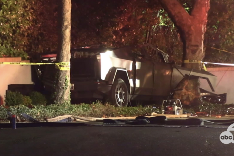 A damaged car is crashed into a tree beside a wall, surrounded by caution tape. It appears to be nighttime, with some debris on the ground.