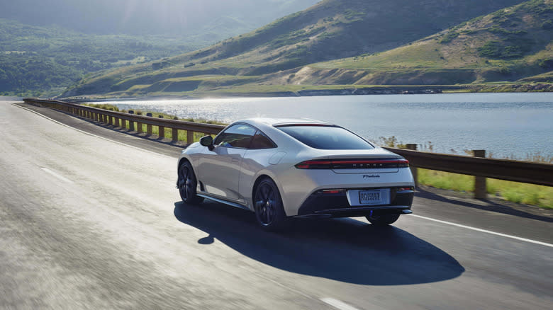 White 2026 Honda Prelude rear 3/4 view driving on a road next to a river in grassy hills