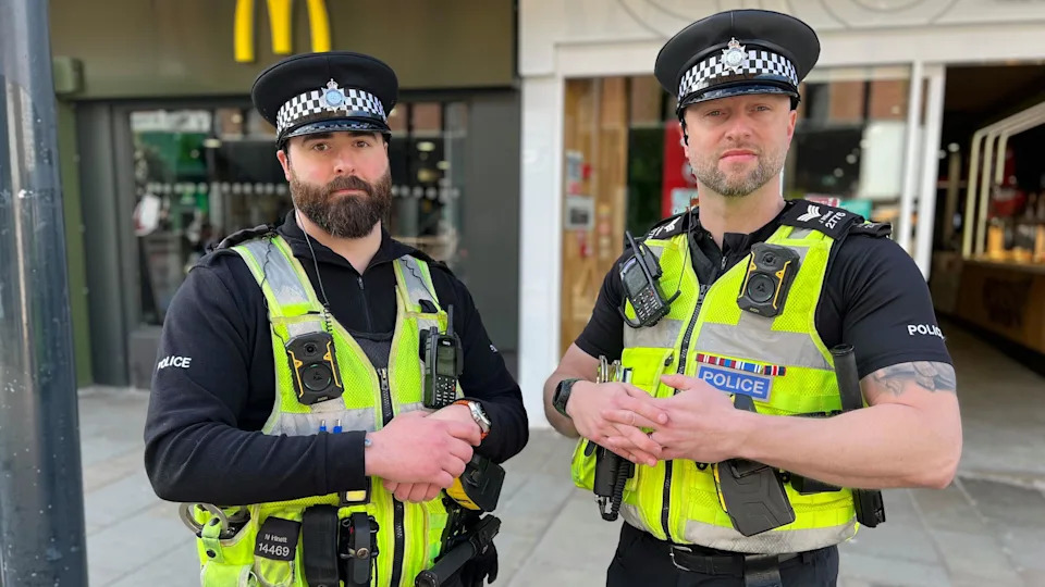 Two policeman stood in city centre high street in neon police vests