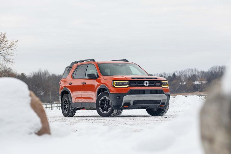 front three quarter view of orange suv parked on snow covered ground with headlights on.
