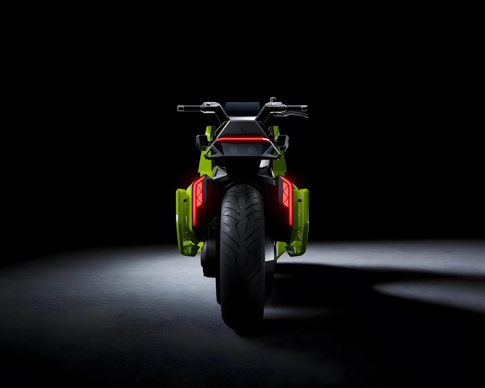 Rear view of a futuristic black and neon green motorcycle with red tail lights on a dark floor.