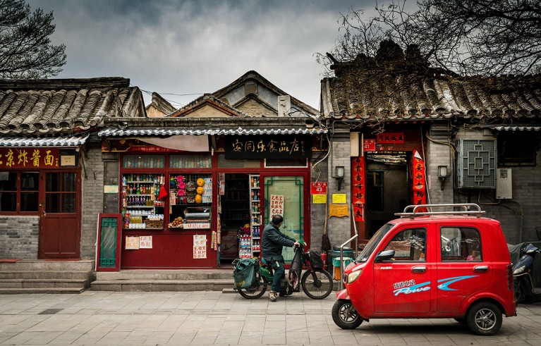 A single small red electric car parked outside traditional single storey buildings with slate roofs on a stree in Beijing.