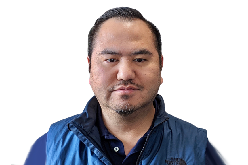 A man in a blue shirt and vest looks at the camera.