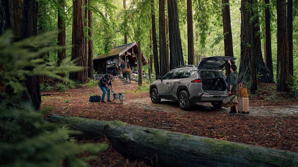 Static rear 3/4 shot of a gray 2026 Toyota RAV4 Woodland parked in a forest with a person open its trunk.