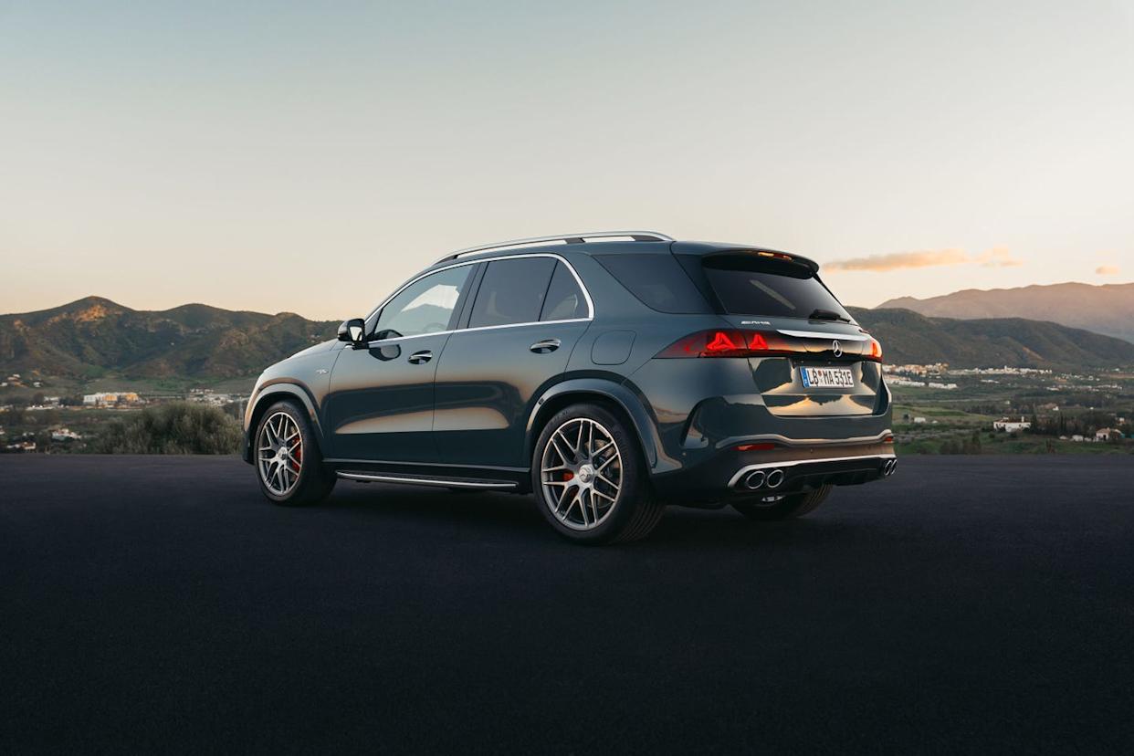 rear three quarter view, dark suv parked on mountain overlook at sunset, valley town and hills in background.