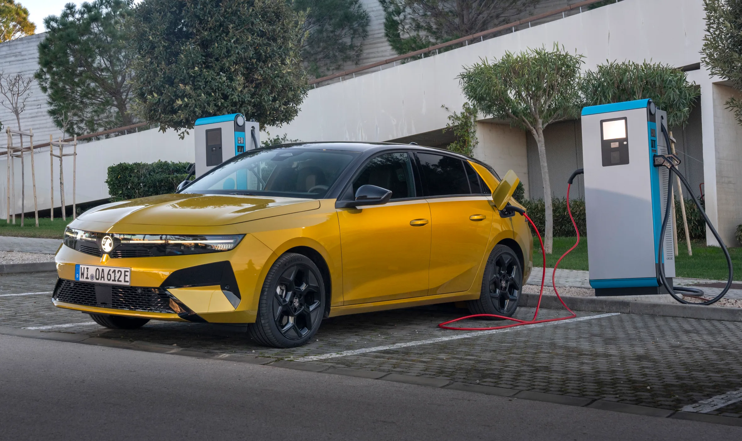 A yellow 2026 Vauxhall Astra Hatch being charged at an electric vehicle charging station.
