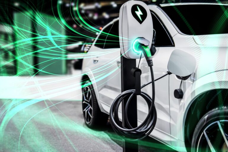 An electric vehicle is charging. The electricity is visible and depicted as green waves traveling to and from the stationary charger.