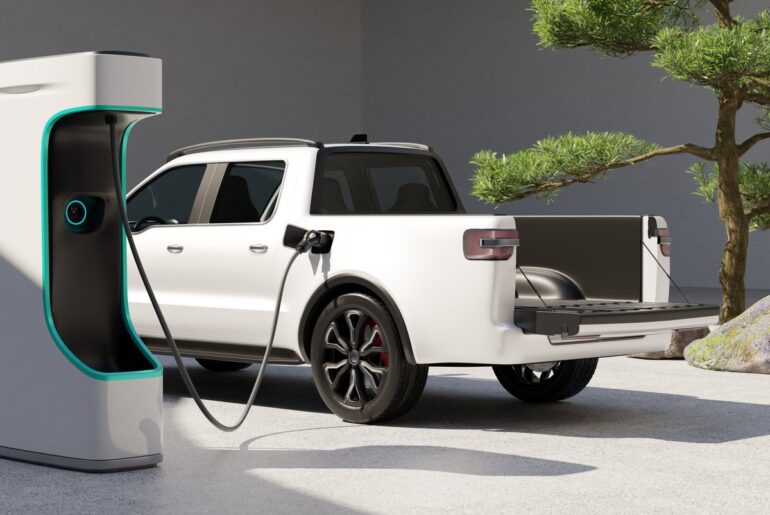 A white electric truck plugged into a charging station.