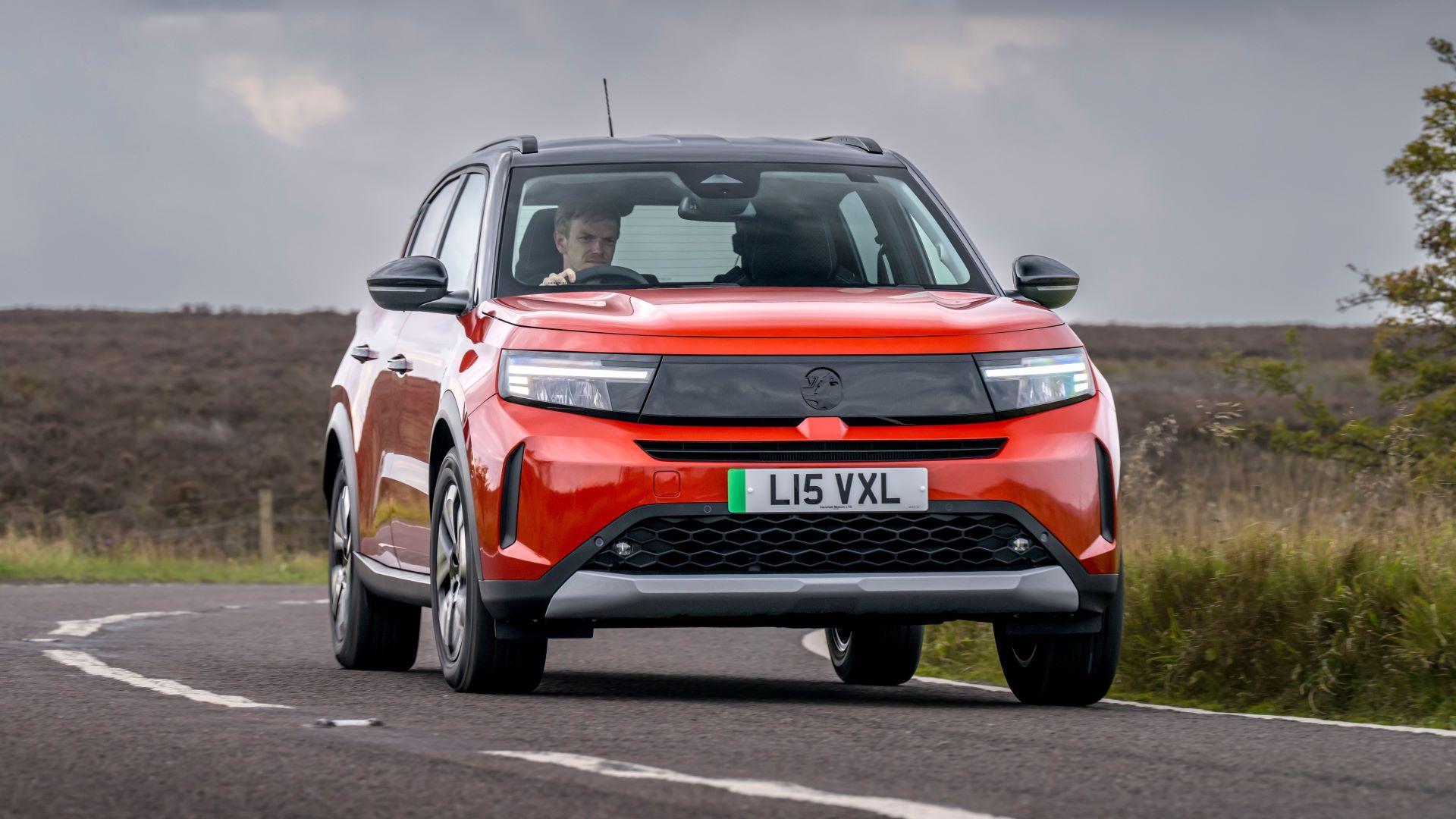 A red Vauxhall Frontera Electric driving round a corner on a rural road.