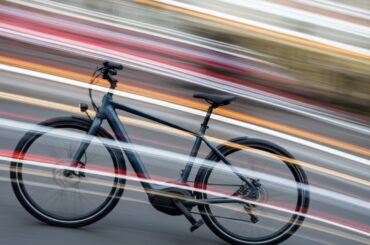 A blurred, abstract image of an electric bicycle in motion, with sweeping streaks of color representing speed and energy.