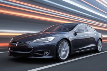 An abstract, blurred image of a Tesla Model S electric vehicle, its form reduced to streaks of vibrant color and motion, representing the company