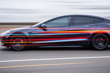 An abstract, motion-blurred image of a Tesla vehicle in vibrant shades of blue, red, and yellow, conveying the speed and technological advancements of autonomous driving while also highlighting the need for human vigilance and understanding of the system