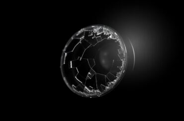 An extreme close-up of a shattered e-bike sensor lens against a pitch-black background, capturing the stark, gritty aftermath of a collision that left a newborn baby fighting for life.
