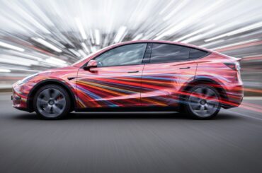 An abstract, motion-blurred image of a Tesla Model Y vehicle, with vibrant streaks of color representing the car's speed and advanced technology.
