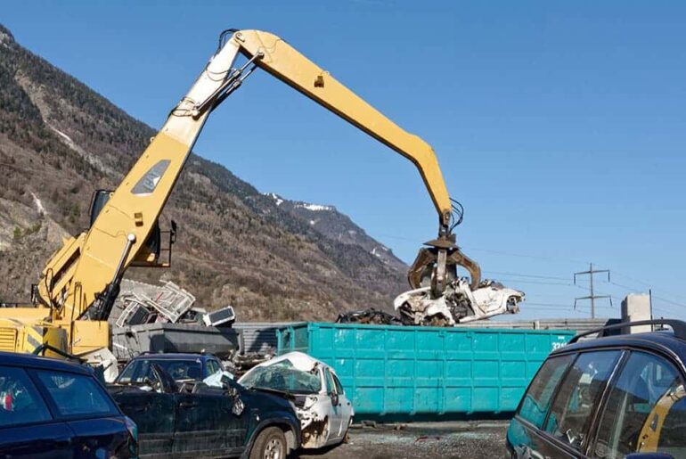 Excavator handling end-of-life vehicles in a recycling yard, illustrating material recovery and processing of scrapped cars.