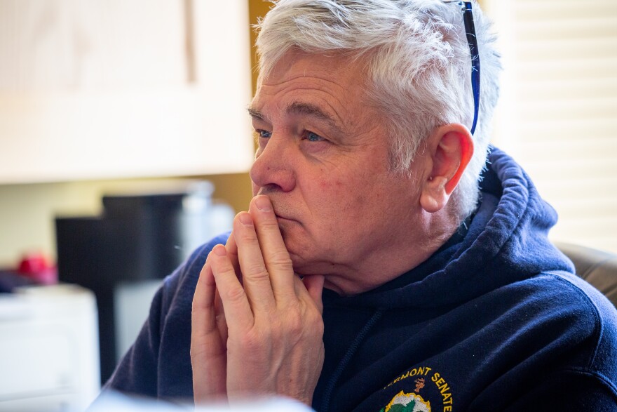 A man wearing a hoodie clasps his hands near his mouth 