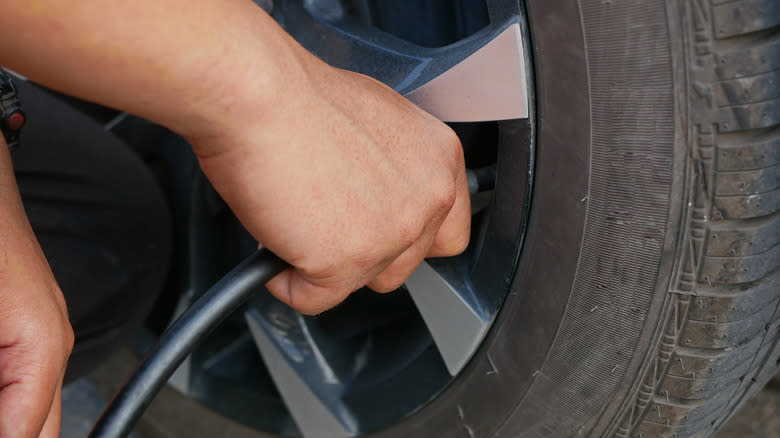 Closeup of a person inflating a car's tire.