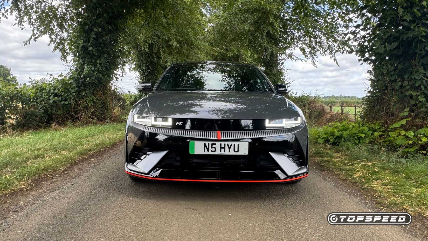 Static front-end shot of a gray 2025 Hyundai Ioniq 5 N parked on a country road lined by trees.