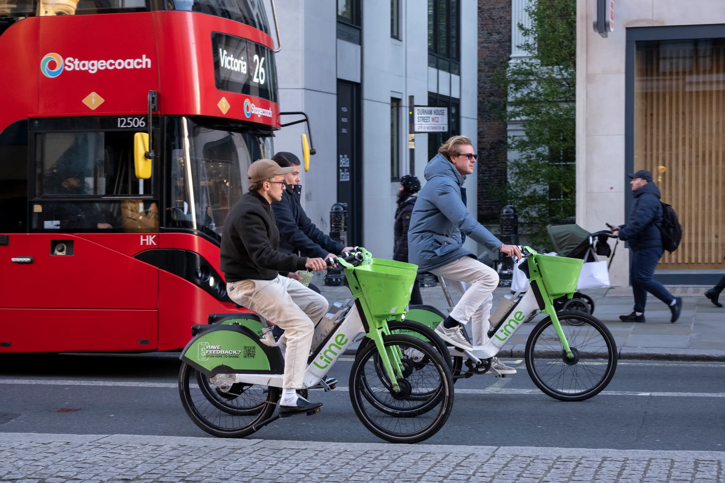 Two men on Lime electric bicycles ride past a red Stagecoach bus in London.