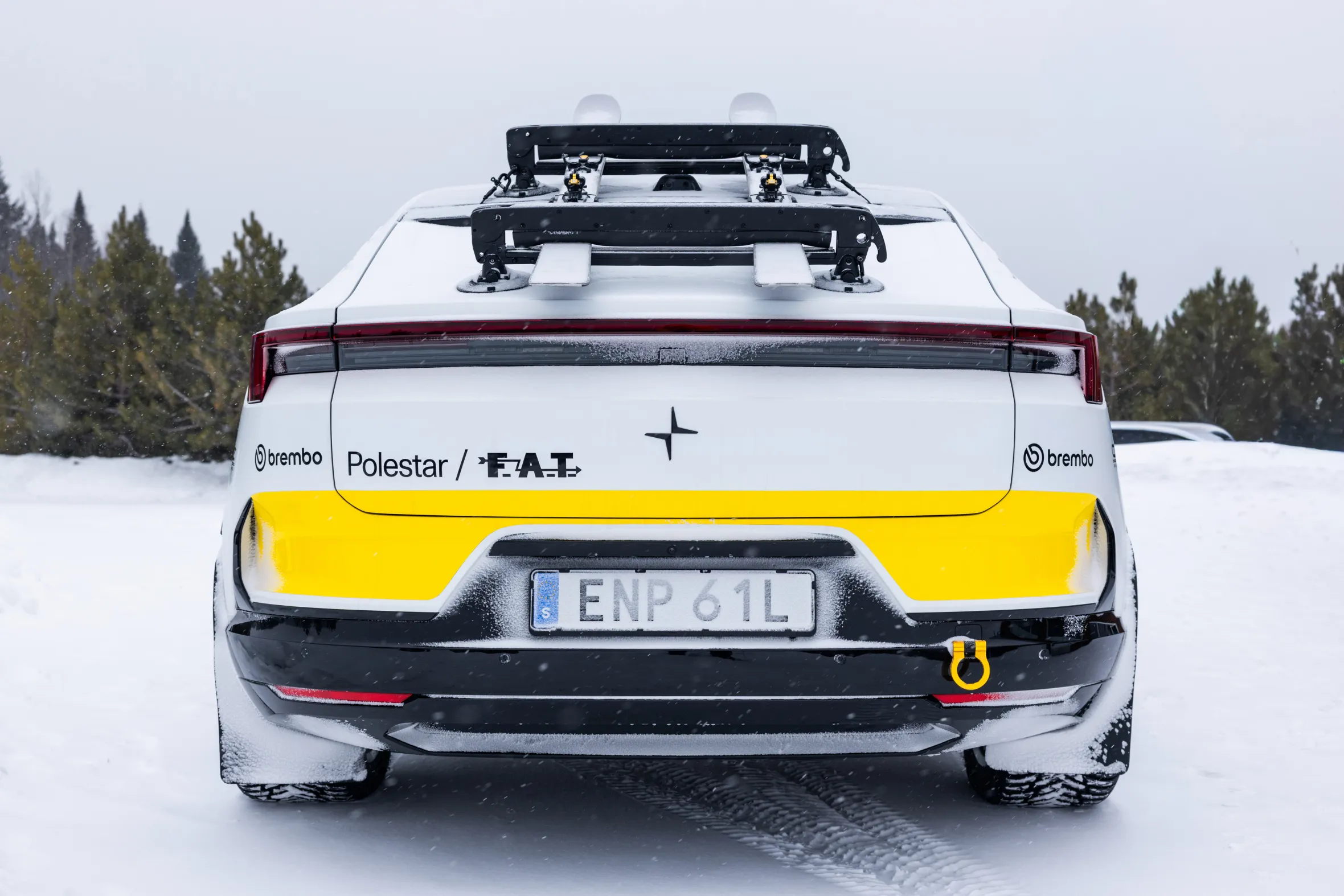 Rear view of a white Polestar 4 with a yellow stripe on the lower tailgate, parked in a snowy landscape.