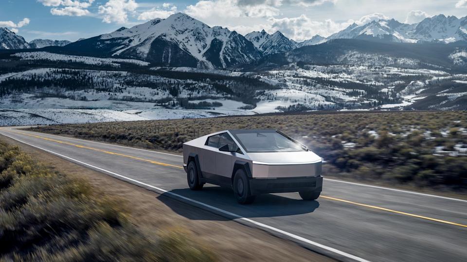 Tesla Cybertruck on a highway with snow-capped mountains in the background.