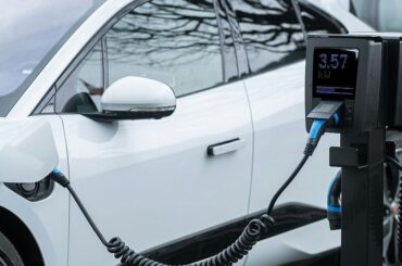 White electric car connected to a black EV charging station with digital display showing 3.57 kW energy delivery