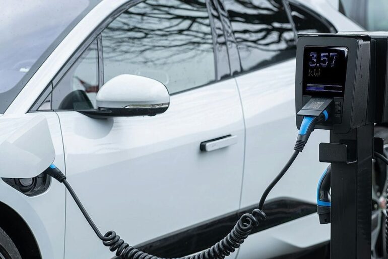 White electric car connected to a black EV charging station with digital display showing 3.57 kW energy delivery