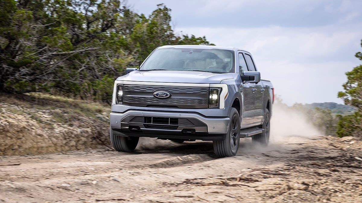 Silver Ford F-150 Lightning Lariat electric truck driving head-on on rocky off-road dirt trail kicking up dust