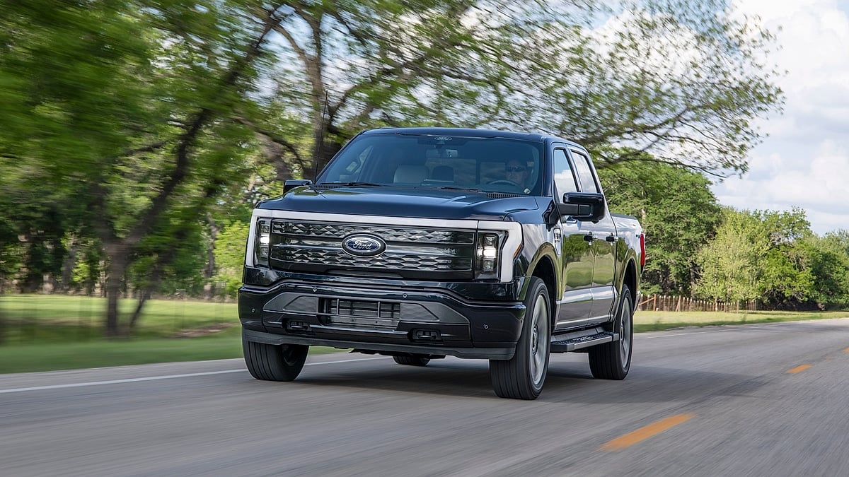 Black Ford F-150 Lightning Platinum electric truck driving on tree-lined country road in front three-quarter view