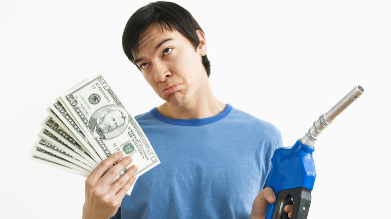 An unhappy man holding money and a fuel pump nozzle