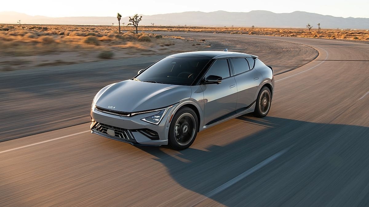 Silver Kia EV6 GT electric vehicle driving on desert road at golden hour seen from front three-quarter angle