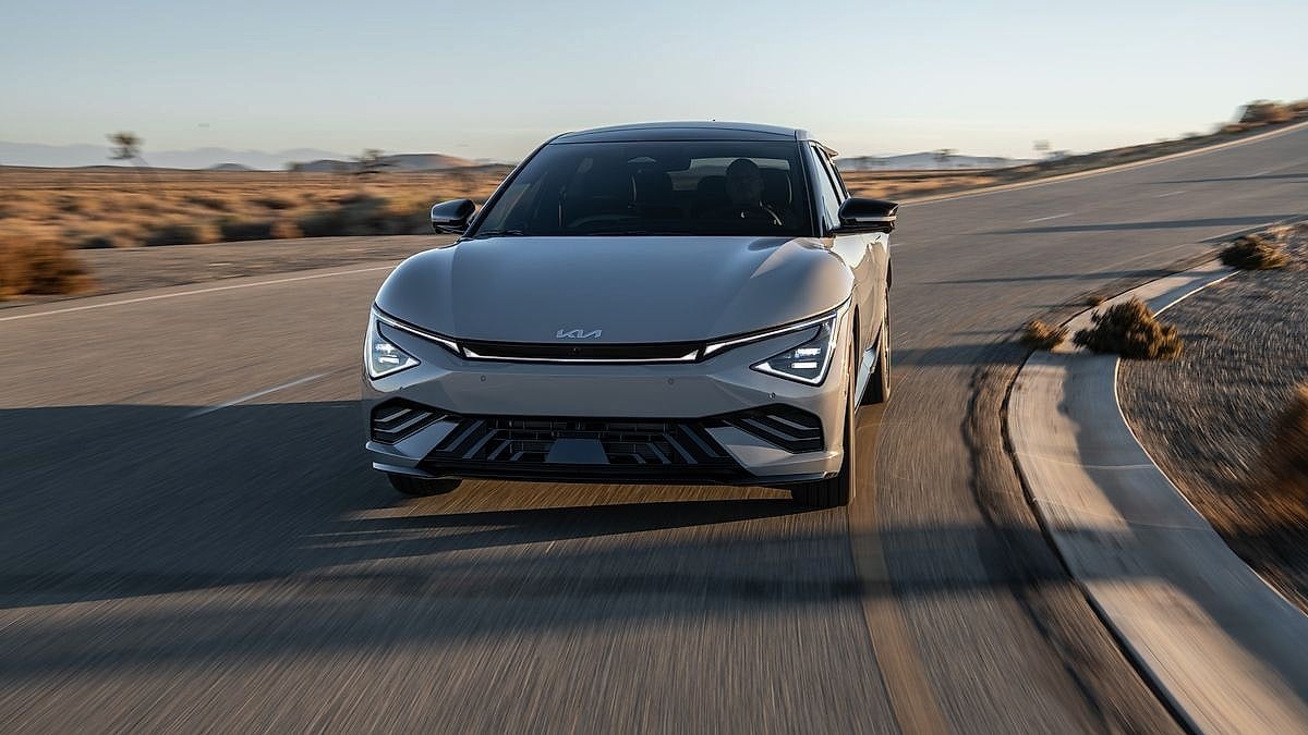 Silver Kia EV6 electric sedan driving head-on down desert highway at dusk with motion blur background