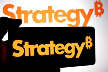 In this photo illustration, a Strategy logo is seen displayed on a smartphone ans in the background.