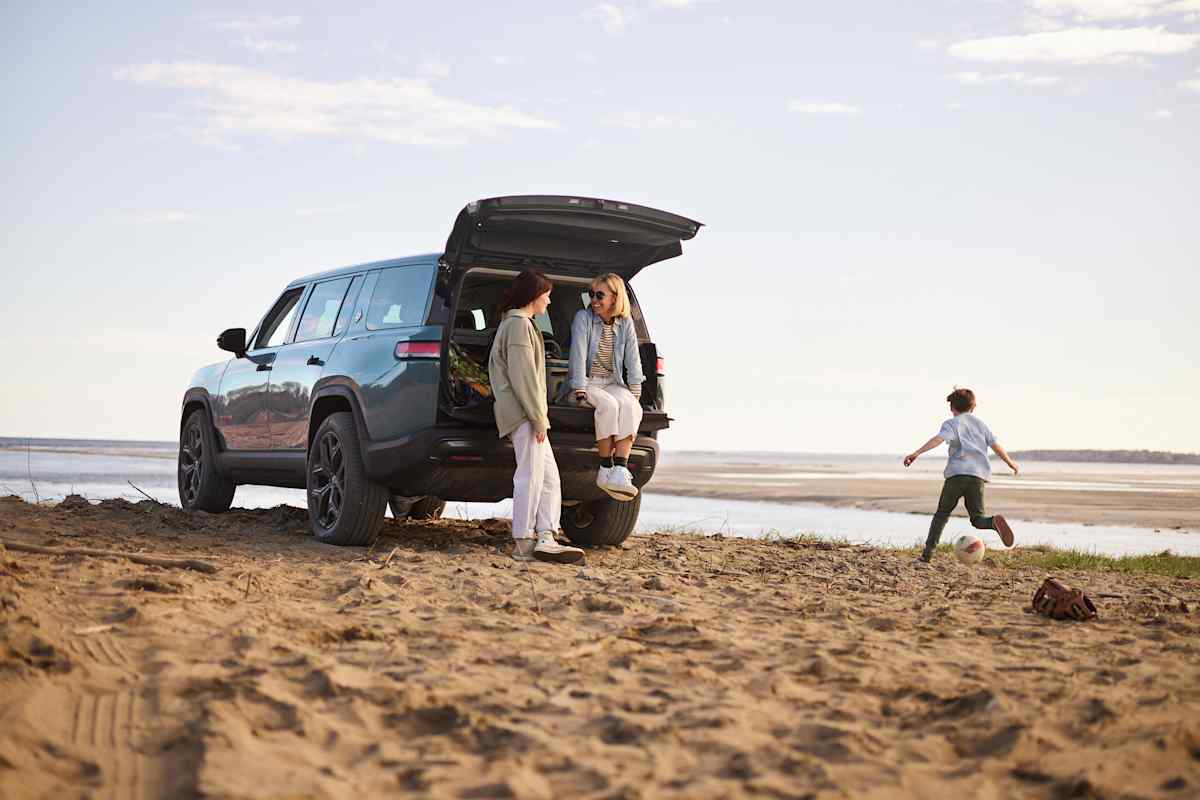 2026 Rivian R1S with rear hatch open at beach, family loading gear while child plays