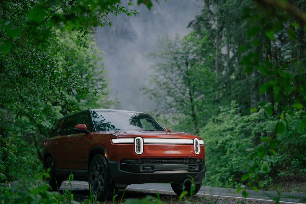 2026 Rivian R1S in red finish driving through misty green forest