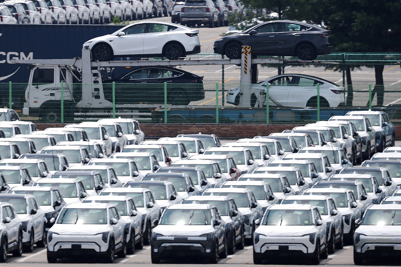A car carrier transporting Tesla vehicles passes by Kia cars parked at a port in Pyeongtaek, Gyeonggi Province. (Yonhap)