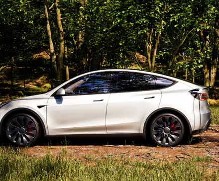 A white Tesla Model Y small electric SUV is charging outdoors. 