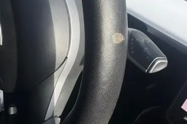 A defective Tesla steering wheel made from plastic vegan leather is shown peeling