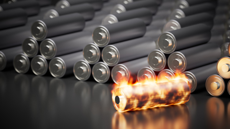 A lithium-ion battery cell on fire in front of stacks of lithium-ion batteries