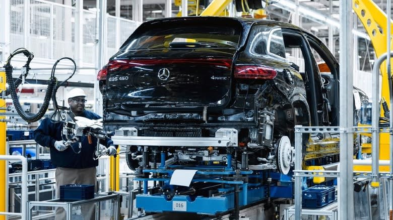 A person works on a Mercedes-Benz being built in a factory.