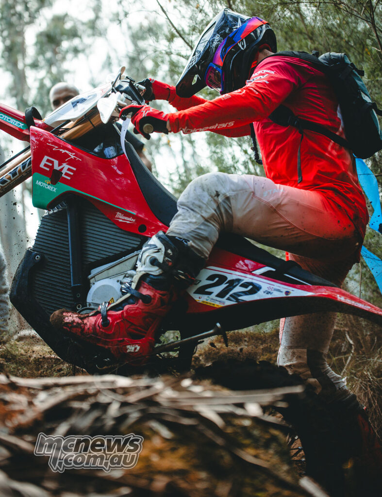 Stark VARG electric off-road motorcycle being ridden through tight bushland terrain.