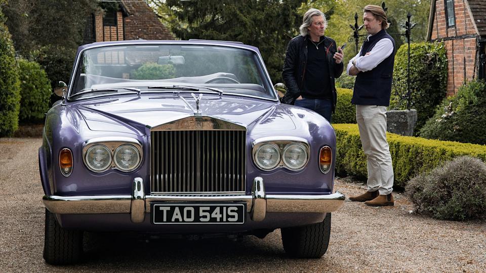 Classic car with two individuals conversing beside it.